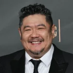 AFP via Getty Images A man in a dark suit with a close-cropped goatee smiles at a premiere