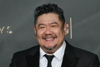 AFP via Getty Images A man in a dark suit with a close-cropped goatee smiles at a premiere