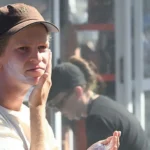 Getty Images A man wearing a white T-shirt and a brown baseball cap puts sunscreen on.