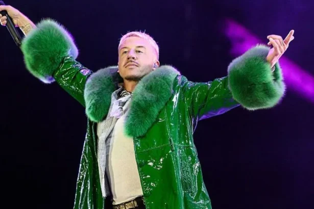 Getty Images Macklemore, who has short, blond hair and short, dark stubble, raises his hands in the air as he holds a microphone while performing on stage. He wears a green coat with fur-type material around the neck and cuffs.