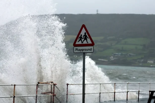 Reuters A wave crashing up onto a path with a metal railing and a black chair. There is a red and white triangular playground sign.