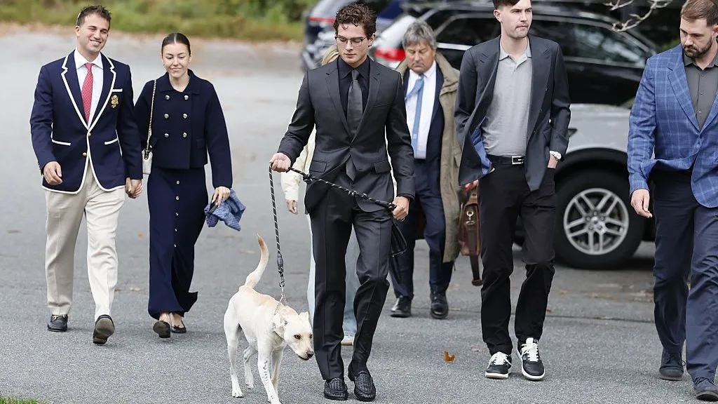 Getty Images Braden Peters, known as Clavicular, is wearing a black suit and walking in a parking lot with entourage and a dog on a leash