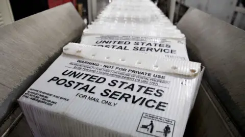 Bloomberg via Getty Images Stacks of United States Postal Service (USPS) flat tubs sit on a conveyor belt