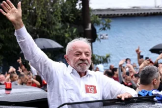 Getty Images Lula is pictured with the upper part of his body from the roof of his car,  wearing a white shirt extends his right arm to greet hundreds of supporters