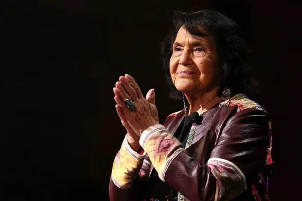 Getty Images Dolores Huerta slightly turned to her right with her hands in a prayer position and a large turquoise ring on her right hand wears a brown leather jacket and long earrings
