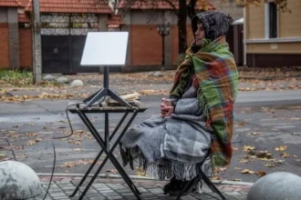 Reuters A man, with at least three blankets around him and a drink in his hand, sits on a chair on the side of a street. Next to him is a small picnic table with a starlink terminal on it.