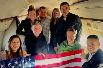 US Government / Handout via REUTERS Stephen Hubbard (second from left in the first row) poses with family members and American officials on board a flight to the US after his release from prison. Photo: 21 October 2026