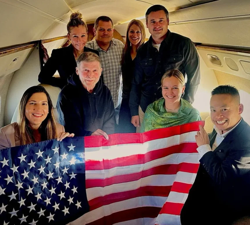 US Government / Handout via REUTERS Stephen Hubbard (second from left in the first row) poses with family members and American officials on board a flight to the US after his release from prison. Photo: 21 October 2026