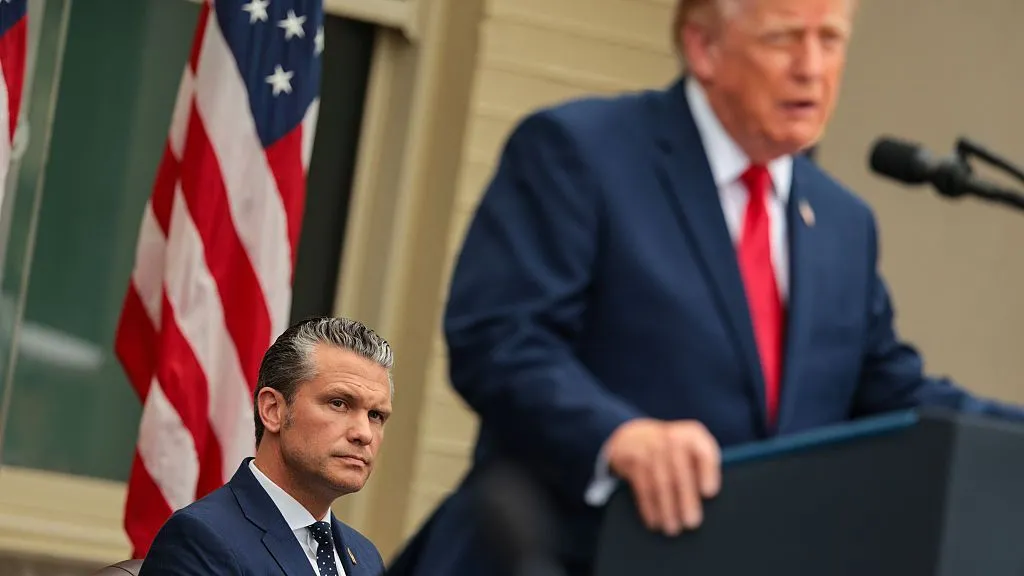 1b9a6640-cd74-11f1-bbdb-c39c91930f26-jpg Getty Images Pete Hegseth seated while President Trump stands at the lectern in a blue suit and red tie