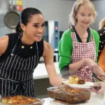 Getty Images Meghan Markle smiles while she serves lunch to a woman