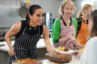 Getty Images Meghan Markle smiles while she serves lunch to a woman