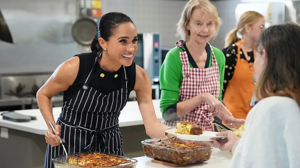 1cb54f90-d1bb-11f1-8746-37a49ff44886-jpg Getty Images Meghan Markle smiles while she serves lunch to a woman