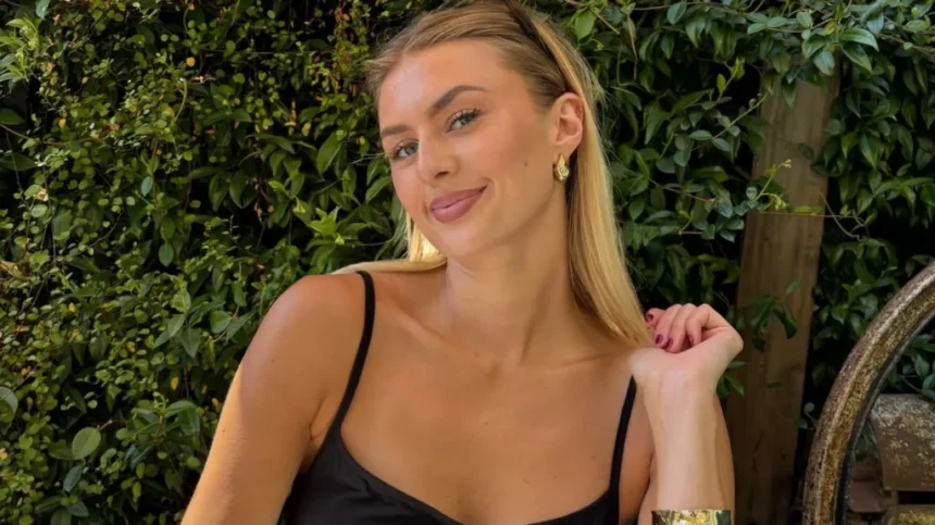 BBC Young woman with long blonde hair smiling, wearing a black dress, with green foliage in the background.