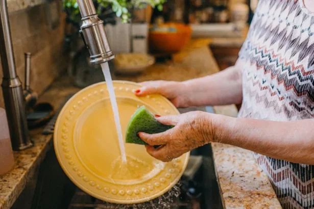 Getty Images A woman with red nail polish stands over the sink washing a yellow plate. She is wearing a patterned top and can only be seen from her waist to her shoulders.