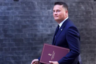 EPA Wes Streeting walks in front of the Downing Street building facade carrying a binder that says 'Secretary of State for Defence' on the front, in September.