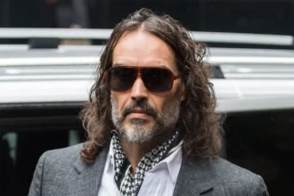 Getty Images Russell Brand arriving at court on Monday 26 October - he is wearing a grey suit jacket, white shirt and black and white cravat. He is also wearing sunglasses.