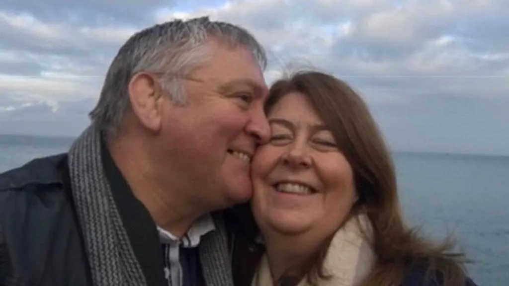 Louisa Nicoll A selfie of John kissing Louisa on the cheek they are both wrapped up warm in coats and scarves and smiling as the wind blows their hair with a blue cloudy sky and sea behind them