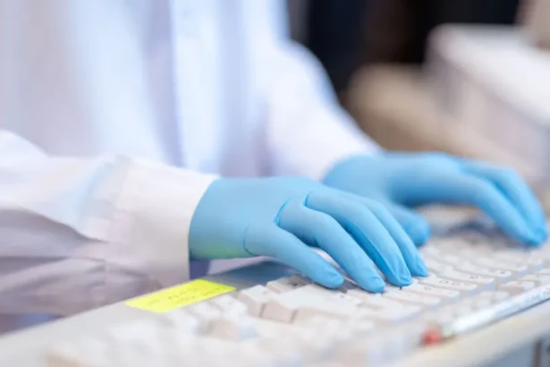 Getty Images A close-up stock image of a lab worker, wearing a white coat and blue gloves, typing on a keyboard.