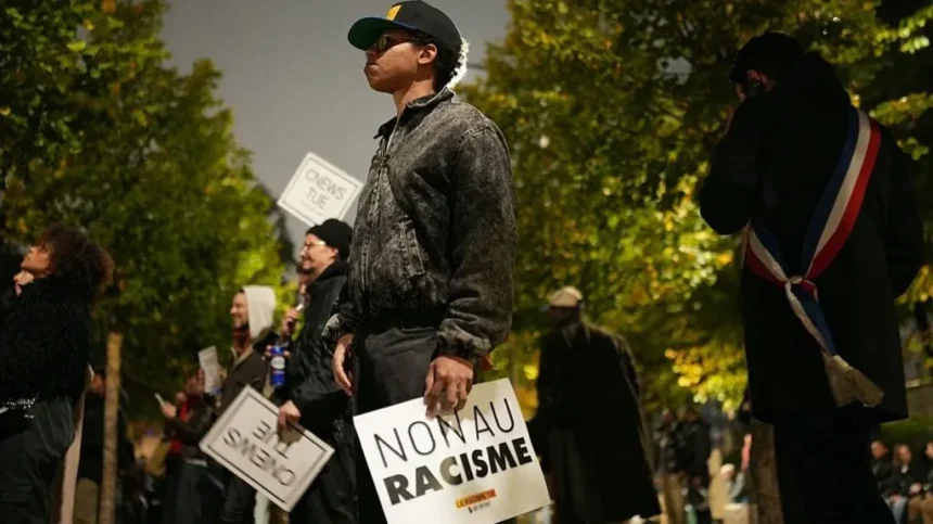Getty Images A man stands solemnly in a line of people holding anti-racism signs. His sign says 'non au racisme'