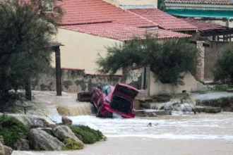 AFP via Getty Images A damaged red car, lying at an angle with its boot open, in a flooded area