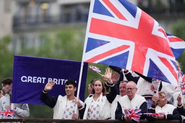 PA Media Tom Daley and other members of Team GB wave from a boat in Paris holding an enormous Union Jack flag aloft, with a Great Britain banner on purple cloth can be seen behind them