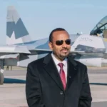 Abiy Ahmed/Facebook Abiy Ahmed, in a black suit and red tie  standing on tarmac in front of a fighter jet