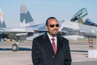 Abiy Ahmed/Facebook Abiy Ahmed, in a black suit and red tie  standing on tarmac in front of a fighter jet