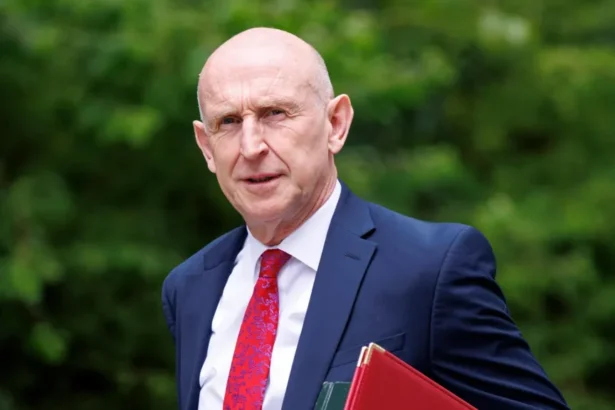 EPA/Shutterstock John Healey walks into Downing Street for a cabinet meeting. He is wearing a blue suit, red tie and white shirt and carries a red, and a green, folder under his arm.