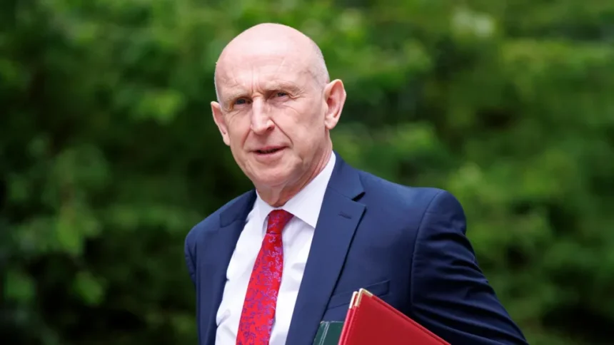 EPA/Shutterstock John Healey walks into Downing Street for a cabinet meeting. He is wearing a blue suit, red tie and white shirt and carries a red, and a green, folder under his arm.