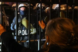 EPA/Shutterstock A woman looks at police officers standing guard outside Poland's Constitutional Tribunal in Warsaw. Photo: 30 October 2026