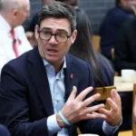 Reuters Andy Burnham sitting at an event in Derby with Chancellor John Healey in the background