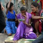 AFP via Getty Images A young female Indian pavement dweller watches a movie on a mobile phone with two other women besides her.