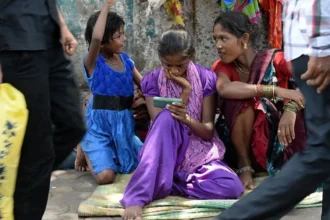 AFP via Getty Images A young female Indian pavement dweller watches a movie on a mobile phone with two other women besides her.