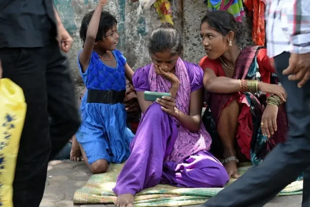 AFP via Getty Images A young female Indian pavement dweller watches a movie on a mobile phone with two other women besides her.