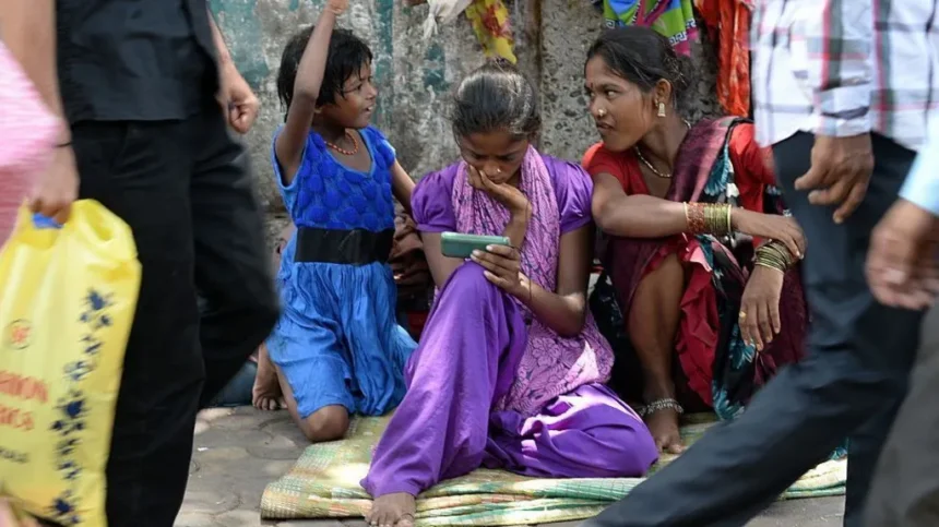 AFP via Getty Images A young female Indian pavement dweller watches a movie on a mobile phone with two other women besides her.