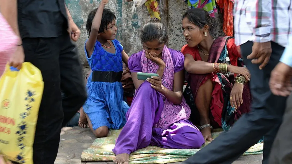 AFP via Getty Images A young female Indian pavement dweller watches a movie on a mobile phone with two other women besides her.