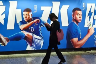 CFOTO/Future Publishing via Getty Images Pedestrians pass by an electrolyte drink advertisement for French football player Kylian Mbappé in the subway in Shanghai, China on June 30, 2026
