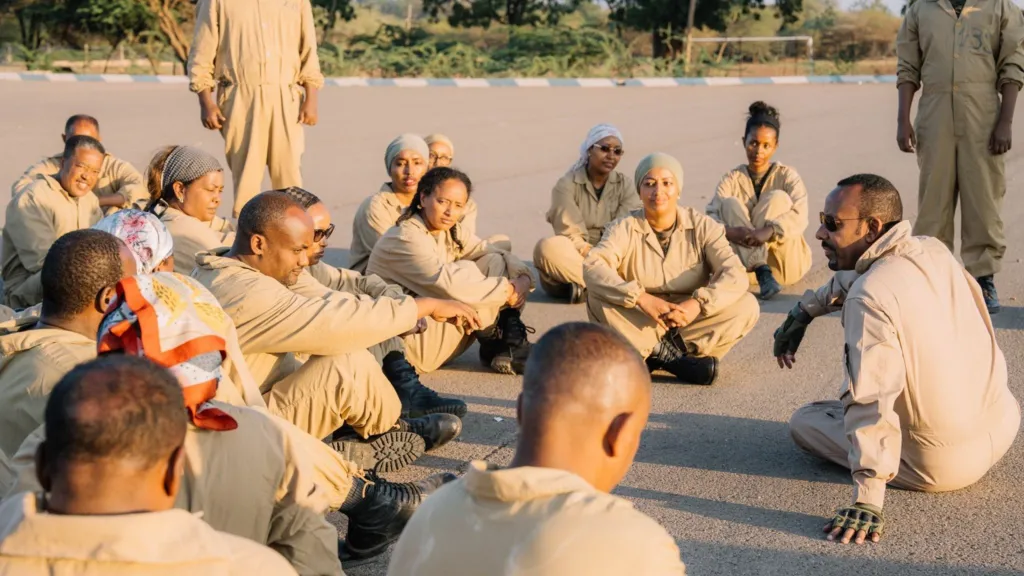 55b5ceb0-d534-11f1-b64c-03717a6e5b71-jpg Abiy Ahmed A photo of Abiy Ahmed seated on the ground, while wearing brown military attire. He is speaking to a group of people wearing same brown attire, who are also seated on the ground.
