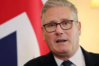 EPA Sir Keir Starmer speaking in front of a union jack flag. It is a head and shoulders shot - he is wearing a white shirt, dark black suit and a dark tie.