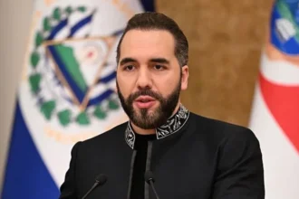 Getty Images Nayibe Bukele in a black jacket with a stitched design around the collar. Two flags are hung behind him.