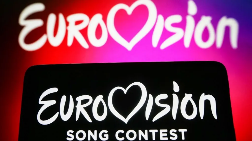 5e717160-d1fd-11f1-b30f-21253679b290-jpg Getty Images Two Eurovision backdrops, one with white words on a pink and red background and the other with white words on a black background in the foreground.