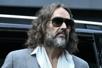 Getty Images Russell Brand in a grey suit, white shirt and long, white scarf, leaving a car to enter the court room