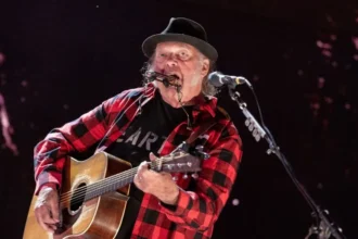 Getty Images Neil young wears a red and black checked shirt and plays a guitar.