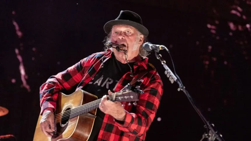 Getty Images Neil young wears a red and black checked shirt and plays a guitar.