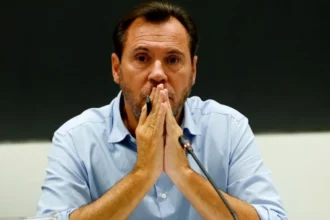 EPA A middle-aged man in a light blue button-down shirt, placing his hands together in a prayer position in front of his mouth while sitting in front of a microphone at a press conference.