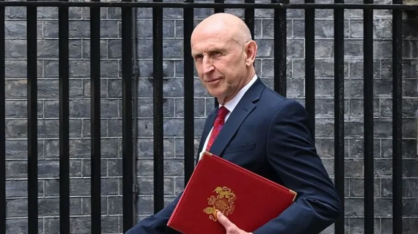 Getty Images Chancellor John Healey walks outside, wearing a navy suit with a red tie. He is holding a red folding and is looking to the side. Behind him is a brick wall and black railings.