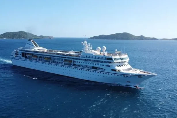 Villa Vie Residences A large white cruise ship sails through deep blue ocean waters near a chain of green, hilly islands under a clear sky.