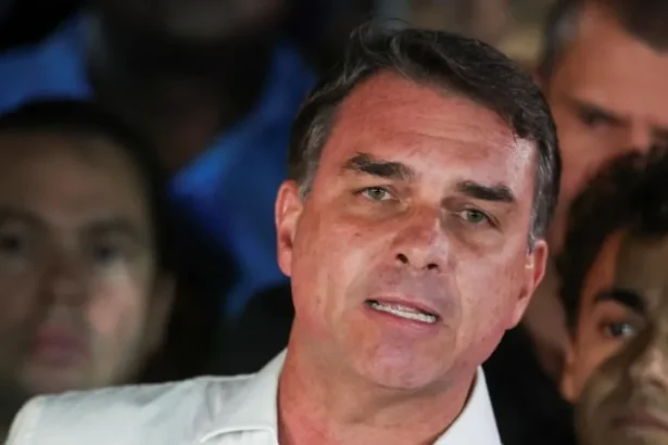 REUTERS/Adriano Machado Brazilian presidential candidate Flavio Bolsonaro of the Liberal Party speaks after losing the presidential runoff election, in Brasilia on 25 October, 2026. He is wearing a white shirt with an open collar. He is gesturing with one hand. Behind him, his supporters look on.
