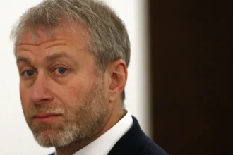 Getty Images Close-up portrait of Roman Abramovich with short grey hair and a neatly trimmed grey beard, wearing a dark suit jacket and white shirt. He is looking slightly over one shoulder toward the camera. The background is softly blurred, with a light-coloured wall and a dark vertical panel visible.