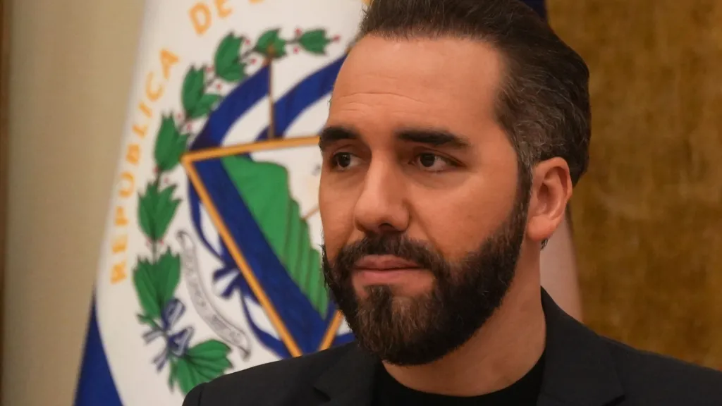 Getty Images Salvadoran President Nayib Bukele wears a black blazer and top during a press conference, with the flag of El Salvador visible behind him.